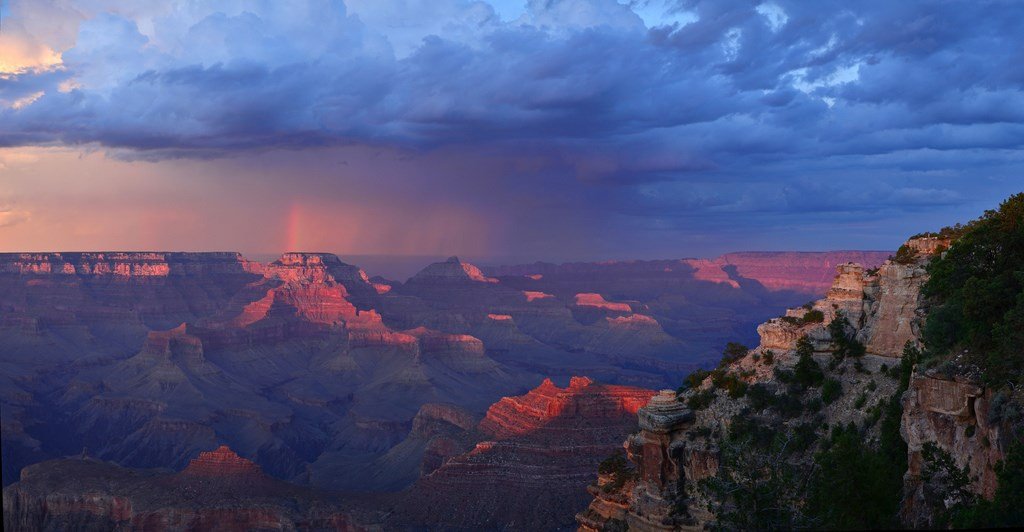Layers of Grand Canyon cliffs glow purple and orange beneath storm clouds.