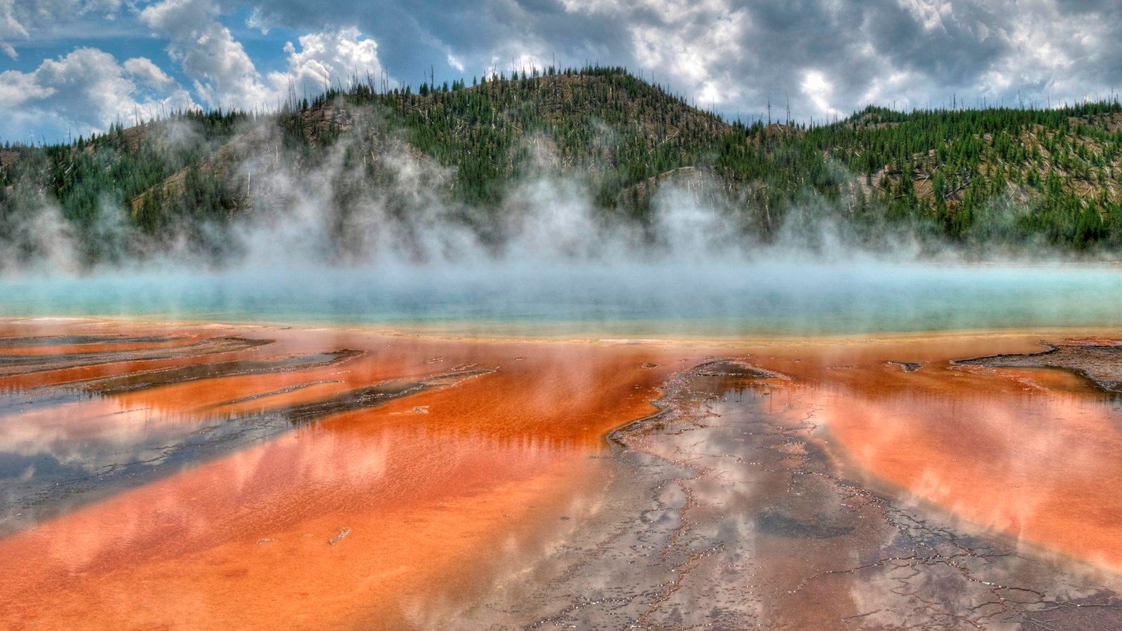 Steam rises above vivid orange and blue Grand Prismatic Spring in Yellowstone.