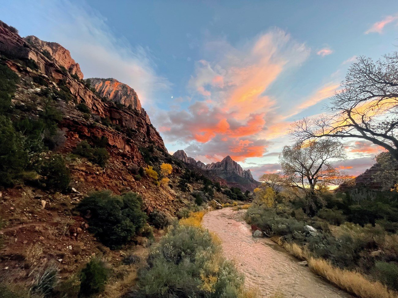 The Virgin River winds between Zion canyon walls beneath sunset clouds.